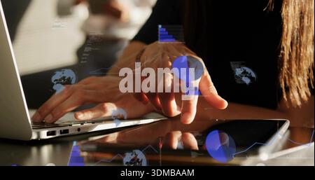 Working mid-adult woman typing on silver laptop while tapping black tablet at desk with data charts Stock Photo