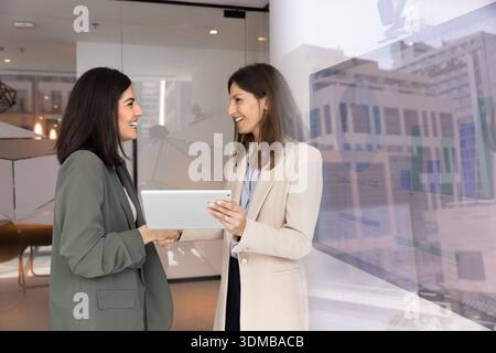 Two professional women smiling, shaking hands while holding digital tablet Stock Photo
