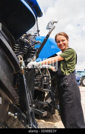 Portrait of female mechanic beside farm tractor Stock Photo