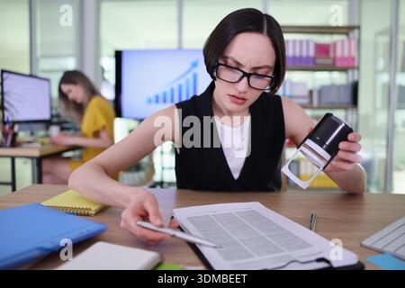 Busy professional reviews important documents while colleague works on a project in a modern office space during daytime Stock Photo