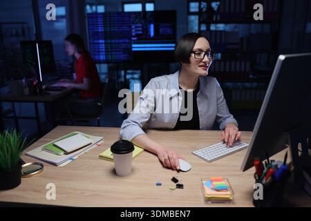 Creative coding session in a modern workspace during nighttime with focused individuals working on computers Stock Photo