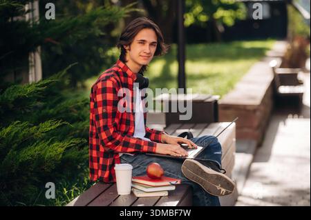 Focused on studying, using laptop. Male student is in the public park outdoors. Stock Photo