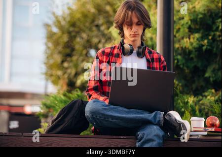 Focused on studying, using laptop. Male student is in the public park outdoors. Stock Photo