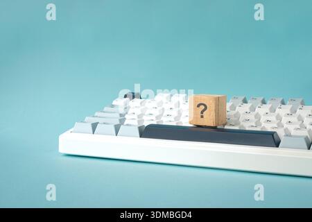 Question mark on wood block on top of keyboard. Isolated on light blue background. Stock Photo