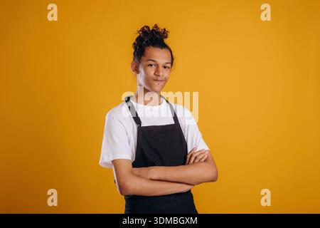 Barista is in apron. Young guy is against yellow background. Stock Photo