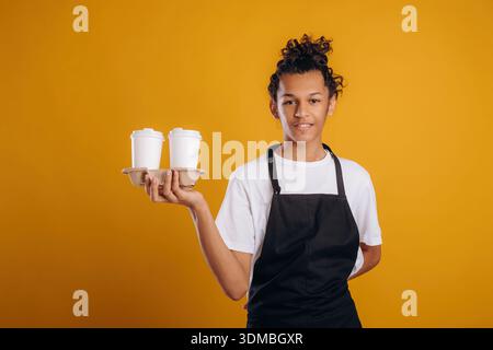 Barista is in apron. Young guy is against yellow background. Stock Photo