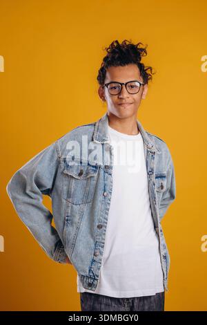 In jean jacket. Young guy is against yellow background. Stock Photo