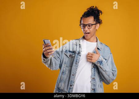 Internet conception, using smartphone. Young guy is against yellow background. Stock Photo