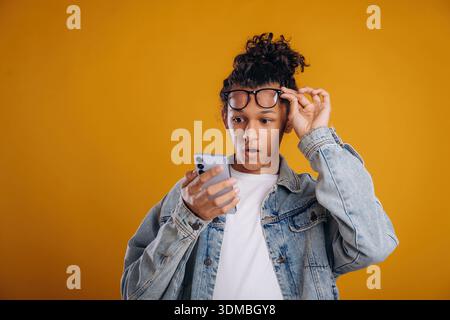 Internet conception, using smartphone. Young guy is against yellow background. Stock Photo