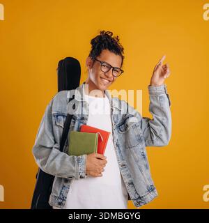 Guitar backpack on back and notepads in hand. Young guy is against yellow background. Stock Photo