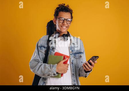 Guitar backpack on back and notepads in hand. Young guy is against yellow background. Stock Photo
