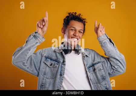 Pointing up by fingers. Young guy is against yellow background. Stock Photo