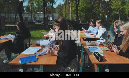 High school students participating in outdoor learning, soaking up the sunshine while working at their desks and interacting with peers Stock Photo