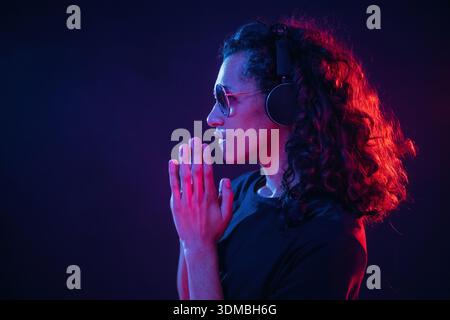 Long hair, headphones, side view. Guy is indoors at night with neon lighting. Stock Photo