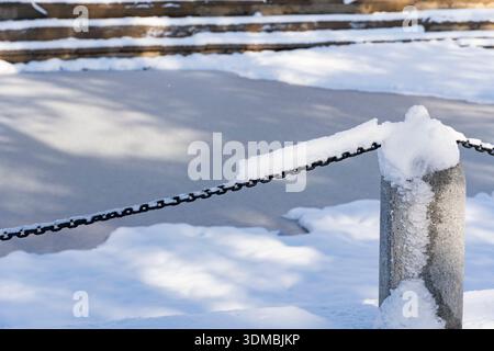 Black metal chain partially covered in snow frames a frozen surface with snowy steps in a quiet winter landscape Stock Photo