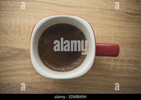 Top view of a coffee in a mug, showing frothy surface and rich brown color in a simple tabletop setting. Stock Photo