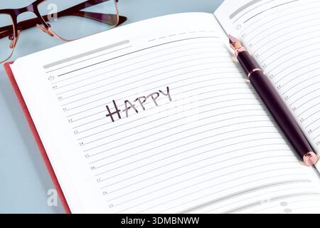 An open red diary shows the word HAPPY handwritten on a white lined page. Stock Photo