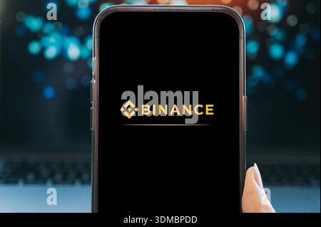Smartphone displaying the Binance logo on a black screen, held in hand with a blurred background. Concept of cryptocurrency trading, digital assets, b Stock Photo