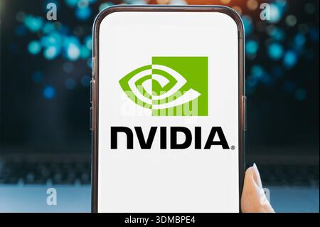 Smartphone displaying the NVIDIA logo on a white screen, held in hand against a blurred technology background. Concept image representing graphics pro Stock Photo