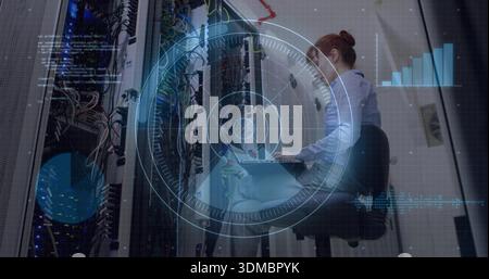 Monitoring woman in button-up shirt working on laptop at server aisle, with racks, HUD, copy space Stock Photo