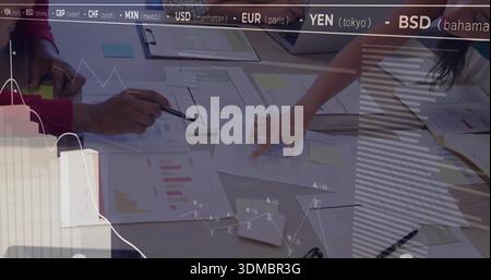 Leaning team analyzing reports at desk, pointing with pen, phone, maroon sleeve, market tickers Stock Photo