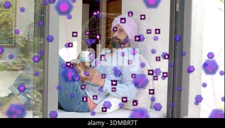 Sitting man with pink turban holding cup and phone by glass door with purple overlay Stock Photo