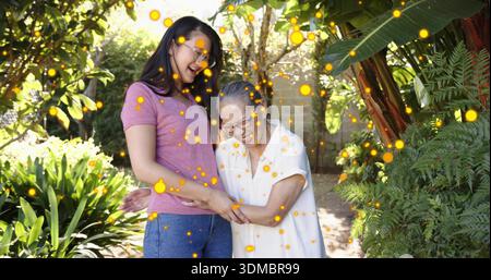 Smiling mid adult woman and senior woman holding hands on backyard path, wearing eyeglasses, bokeh Stock Photo