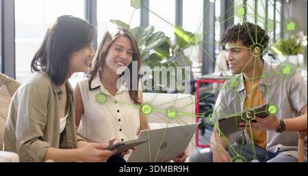 Discussing three coworkers in workwear at coworking lounge, using laptop, tablets, data overlay Stock Photo