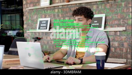 Coding man wearing gray shirt, yellow tee in co-working office, with laptop showing code and tablet Stock Photo