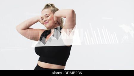 Standing woman wearing black crop top and high-waist bottoms in studio, with digital charts overlay Stock Photo