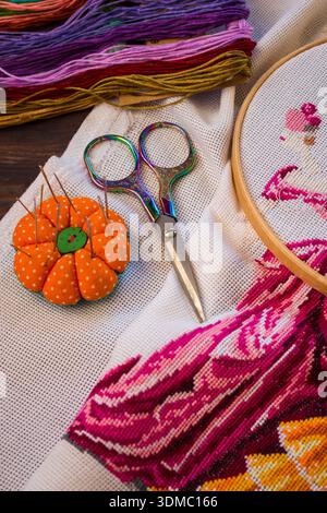 Handmade embroidery with colorful thread on fabric. Scissors, needle, and a pin cushion are placed nearby, emphasizing the craft and needlework proces Stock Photo