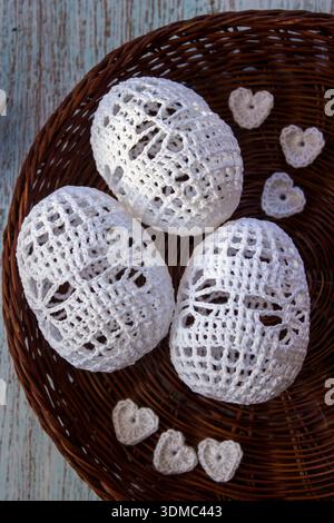 Handmade crochet Easter eggs in a wicker basket with cotton thread and crochet hook on rustic wooden background. Traditional DIY holiday decoration an Stock Photo