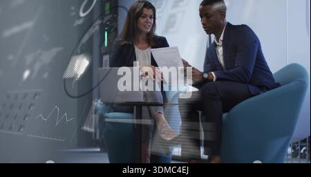 Discussing two professionals in navy suit and dark blazer reviewing document at office with laptop Stock Photo