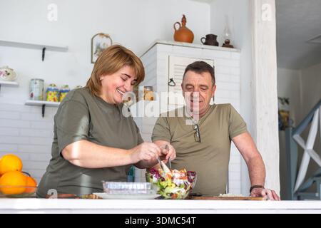 Mature husband and wife cooking fresh meal at home, lifestyle and healthy eating concept. Happy middle-aged couple preparing healthy vegetable salad Stock Photo