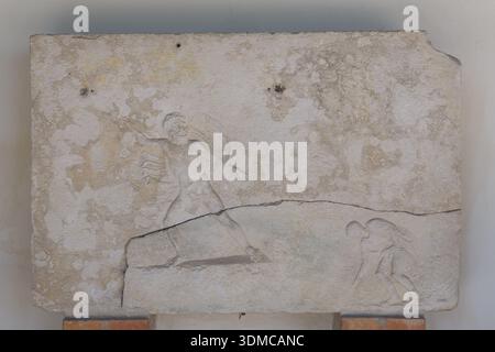 Roman stone relief with carved figures, National Archaeological Museum of Aquileia, Italy. Ancient weathered lapidary art fragment with a cracked surf Stock Photo