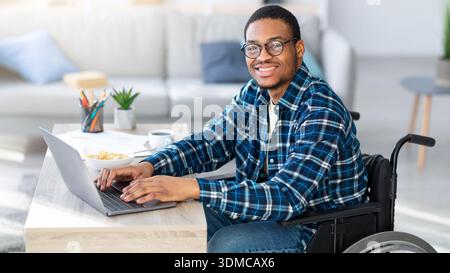 Man Using a Wheelchair Working on Laptop at Home in Modern Living Room Setting Stock Photo