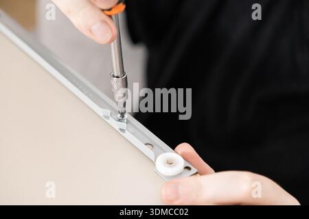 Close-up of human hands performing a delicate assembly task, tightening a small screw on a metal furniture component, ideal for showcasing repair, ren Stock Photo