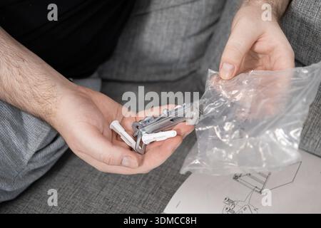 Close-up of a person's hands holding and examining a variety of metal and plastic hardware parts, such as screws, anchors, and wall plugs, for assembl Stock Photo