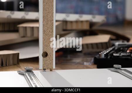 Close-up of a particle board furniture panel showing a cam lock and dowel ready for assembly, with flat-pack components and a toolbox in the backgroun Stock Photo