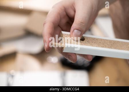 Detailed close-up view of a hand carefully positioning a wooden connecting dowel into a pre-drilled hole of a white furniture panel, emphasizing preci Stock Photo