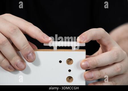 Close-up view of a persons hands carefully joining white flat-pack furniture components by pressing a plastic connector onto pre-drilled dowels, repre Stock Photo