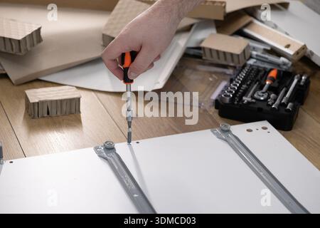 Top-down view of a person assembling white furniture, emphasizing the careful installation of parts with a screwdriver and a toolbox for a home projec Stock Photo