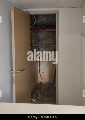 Vertical photograph of an open door, inside there is a small room with pipes and wiring. It's a dirty area in a company locker room. Stock Photo