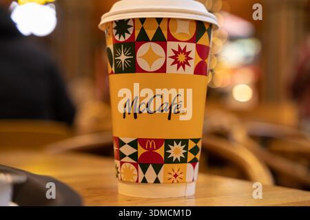 Poznan, Poland - November 19, 2025: McCafe branded yellow takeaway paper coffee cup with festive design, sits on a wooden table, surrounded by soft bo Stock Photo