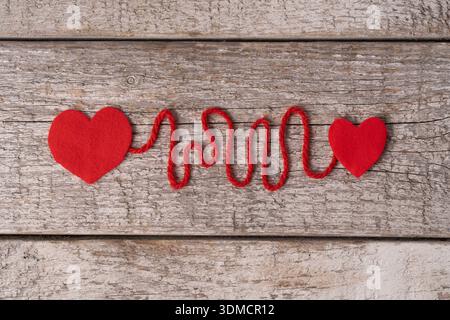 A playful, textured yarn spelling out "LOVE" against a weathered wooden background, flanked by small felt hearts. Stock Photo