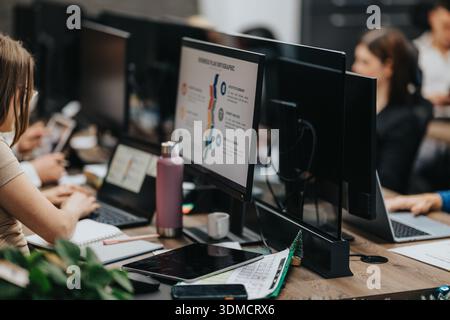 Business workers collaborate at shared desks with multiple monitors and laptops in a modern office Stock Photo