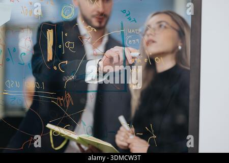 Business professionals analyze complex diagrams on a glass board during a collaborative planning session Stock Photo