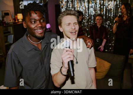 Young Caucasian Man Singing Karaoke with Young Black Man at Party Stock Photo