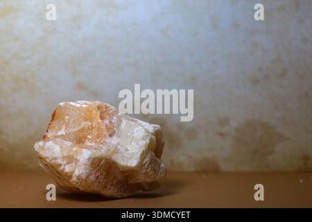 Description: A single raw honey calcite stone placed on a warm-toned surface with a textured background. Stock Photo