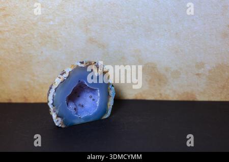 Close-up of a dyed blue agate geode slice with sparkling crystalline interior, placed against a warm beige backdrop. Stock Photo